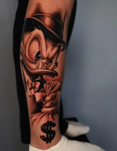 Paperone con dollaro, tatuaggio realistico sulla gamba - Andrew Lead, Keyo Tattoo Studio Locarno